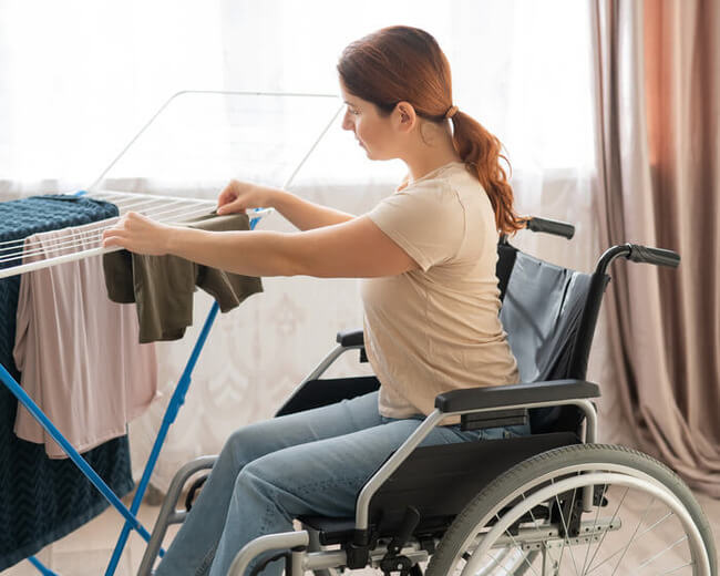 A stay-at-home mom in a wheelchair in her home hanging laundry on a short laundry-drying rack.